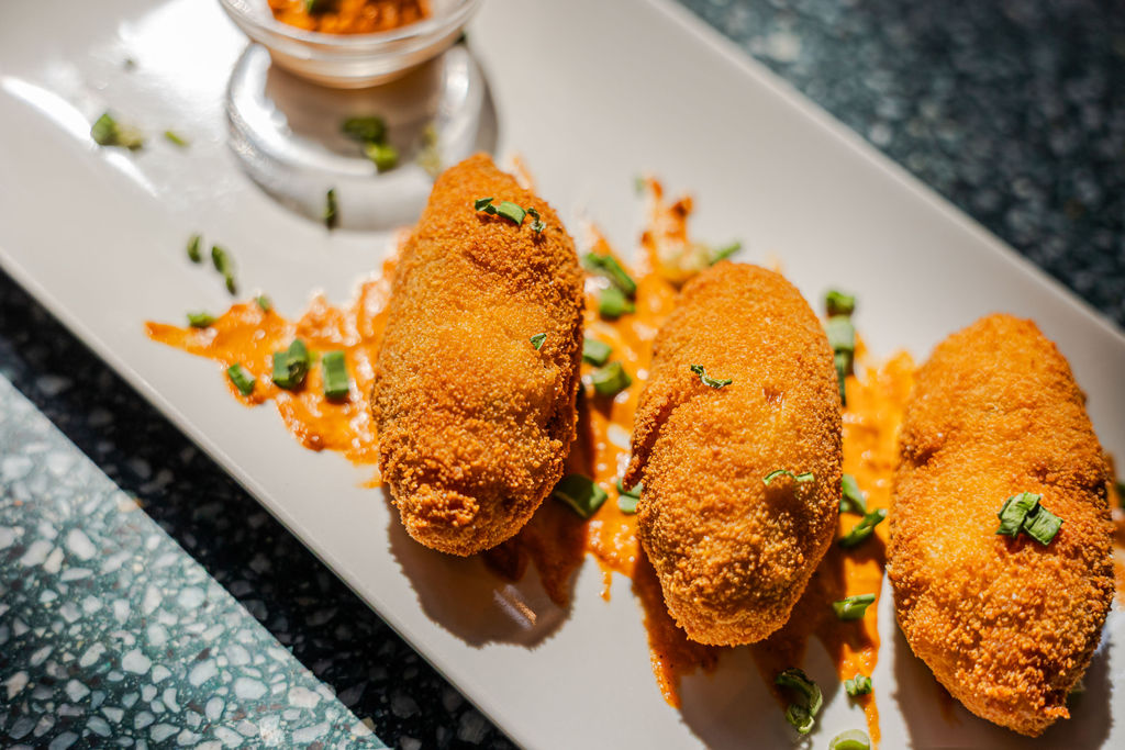 Primer pla de dues croquetes artesanes decorades amb salsa i brots sobre un plat de ceràmica, simbolitzant la cuina de KM 0 i producte del Penedès. Primer pla de dues croquetes artesanes decorades amb salsa i brots sobre un plat de ceràmica, simbolitzant la cuina de KM 0 i producte del Penedès.